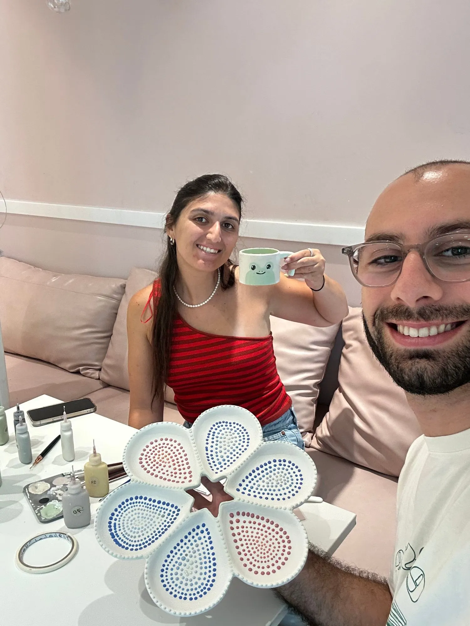 Dana holding up a painted mug beside a flower shaped ceramic plate covered in painted dots
