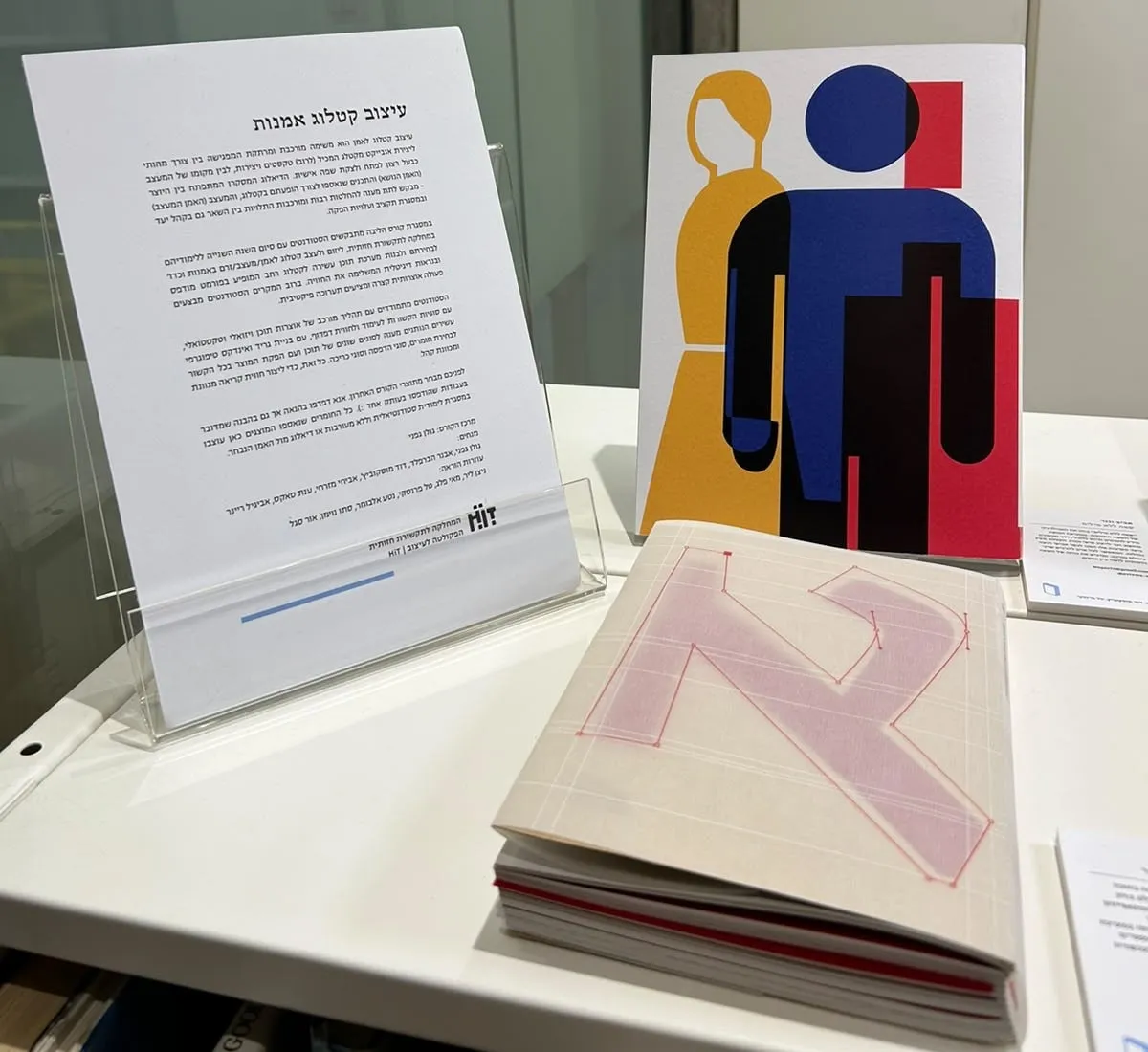 The exhibition text on an acrylic stand, a poster from another catalogue behind it, and the catalogue lying in front