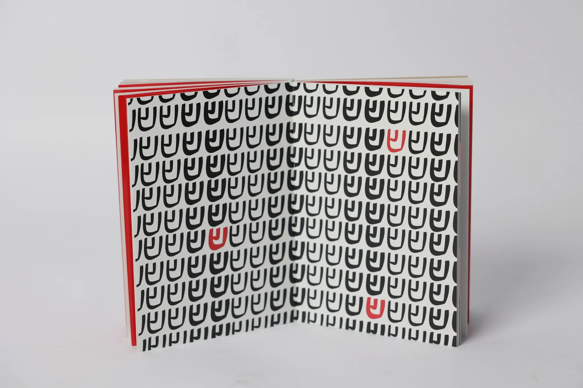An open spread tiled with one Hebrew letter repeated in black across both pages, three of them picked out in red